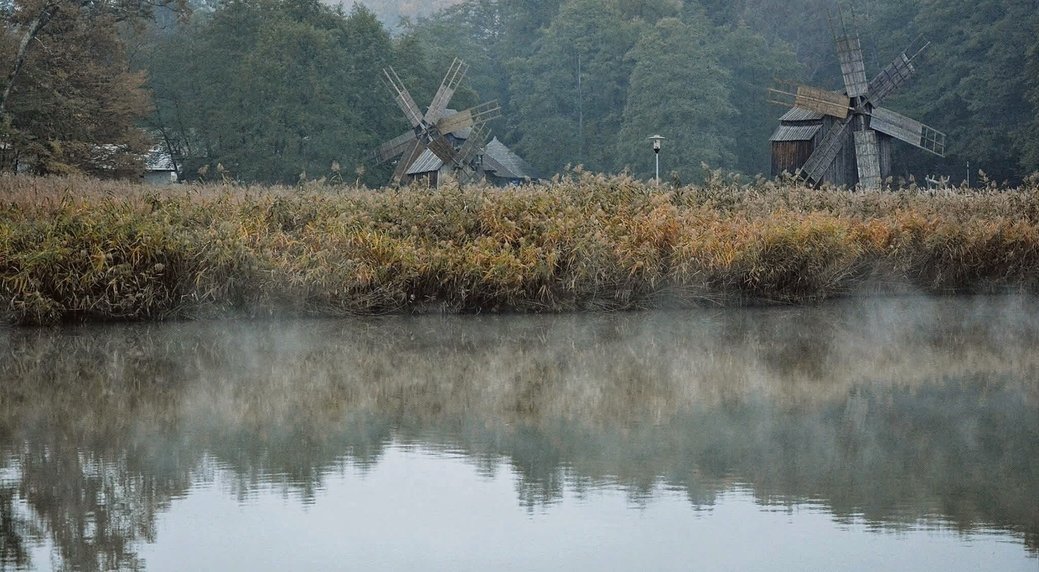 Archival photograph, 2014, Romania; calm water, reed bank and wooden windmills documented during an educational residential plein-air art programme.